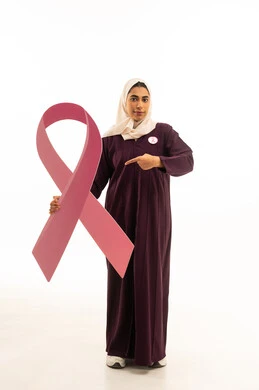 الاشارة الى شعار الحملة العالمية لسرطان الثدى, بورتريه لإمرأة عربية خليجية سعودية محجبة ترتدي العباءة تحمل شعاراليوم العالمي للتوعيه بالكشف المبكر ,الجسم بالطول الكامل, خلفية بيضاء