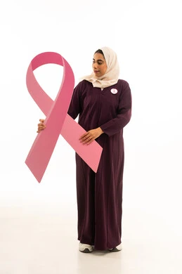 تحدي الأمراض الخبيثة, بورتريه لإمرأة عربية خليجية سعودية محجبة ترتدي العباءة تمسك شعار التوعيه بالكشف المبكر لسرطان الثدي, الجسم بالطول الكامل, خلفية بيضاء