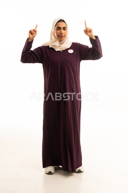 A portrait of a smiling Saudi Arabian Gulf woman wearing an abaya, pointing with her index fingers upwards, indicating the location of something specific, with expressions of certainty and pinpointing a specific place, full-body shot, white background.