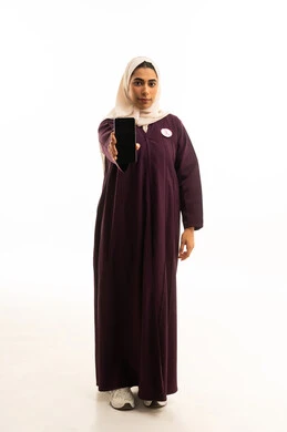 A portrait of a Saudi Arabian Gulf woman wearing a hijab and an abaya, holding a mobile phone in her hand with the global breast cancer campaign logo, displaying a black screen on the phone, full-body shot, white background.
