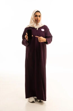 A black screen displayed on a mobile phone, a portrait of a Saudi Arabian Gulf woman wearing a hijab and an abaya, holding a mobile phone in her hand with the logo of the global breast cancer campaign, full-body shot, white background.