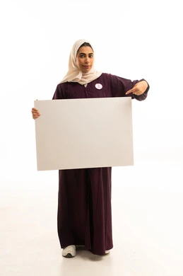 الاشارة الى لوحة توعوية مستطيلة فارغة, بورتريه لإمرأة عربية خليجية سعودية محجبة ترتدي عباءة بنية تحمل بيدها موك اب مستطيل أبيض, الجسم بالطول الكامل, خلفية بيضاء