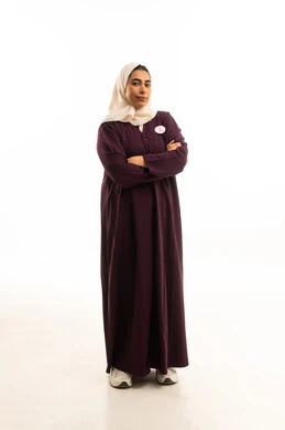 Standing with crossed arms, elegance and attention to external appearance, a portrait of a smiling Saudi Gulf Arab woman wearing a brown abaya and the awareness slogan for early detection of breast cancer, the awareness campaign for the malignant disease, full-body shot, white background.