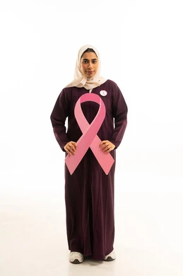 اليوم العالمي للتوعية بالمرض الخبيث بورتريه لامرأة عربية خليجية سعودية مبتسمة محجبة ترتدي العباءة البنية تمسك شعار التوعيه بالكشف المبكر لسرطان الثدي، الحملة التوعويه بالمرض الخبيث، الجسم بالطول الكامل, خلفية بيضاء