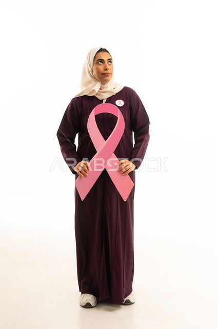 A portrait of a smiling Saudi Gulf Arab woman wearing a hijab and an abaya, looking at something while holding a slogan for the awareness campaign for early detection of breast cancer, the awareness campaign for the malignant disease, full-body image.