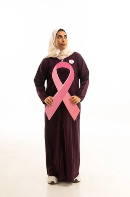 بورتريه لامرأة عربية خليجية سعودية مبتسمة محجبة ترتدي العباءة تنظر الى شىء ما تمسك شعار التوعيه بالكشف المبكر لسرطان الثدي، الحملة التوعويه بالمرض الخبيث، صورة الجسم بالطول الكامل