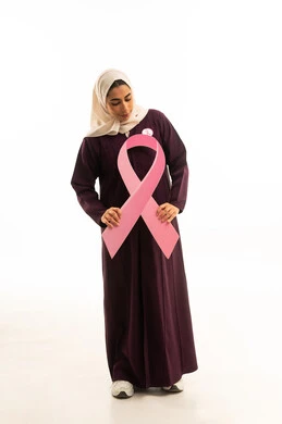 الحملة التوعويه بالمرض الخبيث، بورتريه لامرأة عربية خليجية سعودية مبتسمة محجبة ترتدي العباءة تنظر الى شىء ما تمسك شعار التوعيه بالكشف المبكر لسرطان الثدي، الجسم بالطول الكامل