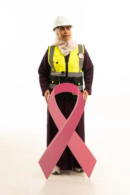 التأمل والنظر للاعلى, اليوم العالمي للتوعية بالمرض الخبيث, بورتريه لمهندسة عربية خليجية سعودية مبتسمة ترتدي سترة الحمايه مع الخوذه تمسك بيديها شعارالتوعيه بالكشف المبكر لسرطان الثدى, الجسم بالطول الكامل, خلفية بيضاء