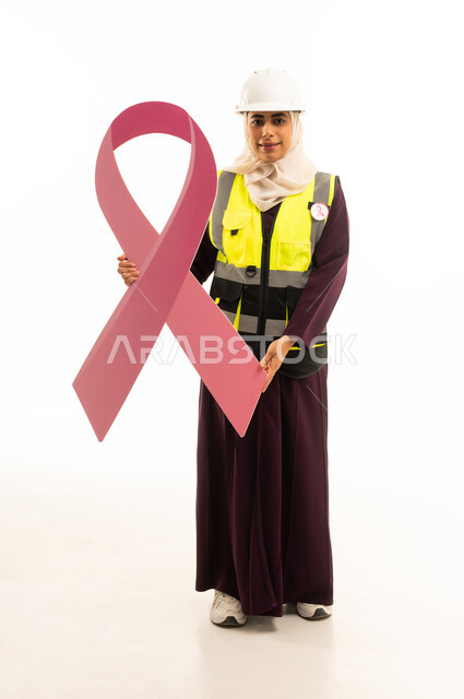 World Cancer Awareness Day, a portrait of a smiling Saudi Gulf Arab engineer wearing a safety vest and helmet, holding in her hands the awareness slogan for early detection of breast cancer, looking at the camera, full body, white background.