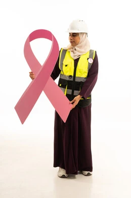 بورتريه لمهندسة عربية خليجية سعودية مبتسمة ترتدي سترة الحمايه مع الخوذه تمسك بيديها شعار التوعيه بالكشف المبكر لسرطان الثدى, الجسم بالطول الكامل, خلفية بيضاء