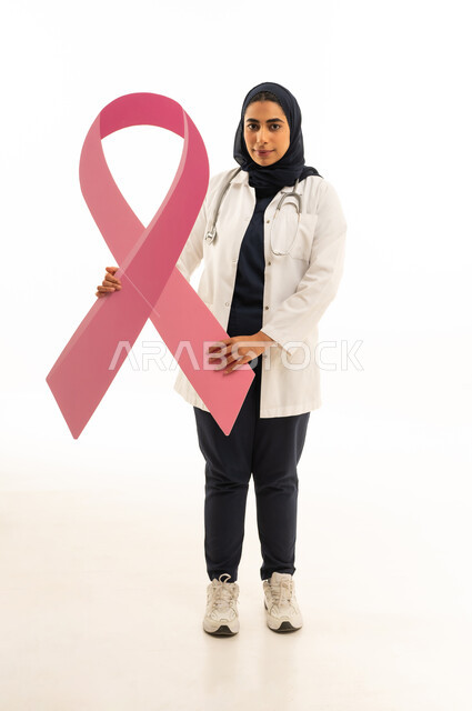 تحدي المرض الخبيث, بورتريه لامرأة عربية خليجية سعودية محجبة ترتدي الزى الكاجوال و السماعة الطبية تحمل شعار التوعيه بالكشف المبكر لسرطان الثدي تنظر الى الكاميرا, الجسم بالطول الكامل, خلفية بيضاء