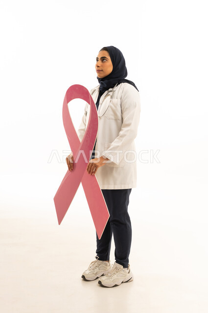 بوتريه من الجانب لامرأة عربية خليجية سعودية محجبة ترتدي الزى الكاجوال تمسك بيديها شعار الحملة العالمية, تقديم المساعدة والدعم من خلال الكشف المبكر عن سرطان الثدي، خلفية بيضاء