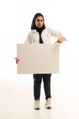 بوتريه لامرأة عربية خليجية سعودية محجبة ترتدي الزى الكاجوال و شعارالحملة العالمية لسرطان الثدى تحمل بيدها موك اب مستطيل أبيض فارغ, لوحة توعوية لمكافحة الاورام, خلفية بيضاء