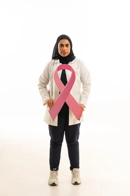 النظر إلى الكاميرا بتعابير الثقة بالنفس,  بوتريه لامرأة عربية خليجية سعودية محجبة ترتدي الزى الكاجوال تمسك بيديها شعارالحملة العالمية الوردى لمكافحة سرطان الثدى بإيماءات الانتصار والنجاح, خلفية بيضاء