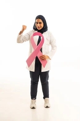 بوتريه لامرأة عربية خليجية سعودية محجبة ترتدي الزى الكاجوال تمسك بيديها شعارالحملة العالمية الوردى لمكافحة سرطان الثدى ترفع قبضة يديها للاعلى بإيماءات الانتصار والنجاح, النظر إلى الكاميرا بتعابير الثقة بالنفس, خلفية بيضاء