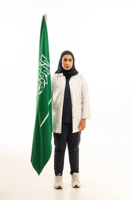 العيد الوطني 23 سبتمبر, مفهوم حب الوطن والانتماء له,  يوم العلم السعودي 11 مارس، بورتريه لامرأة عربية خليجية سعودية محجبة ترتدي الزى الكاجوال تنظرالى علم المملكة, المشاركة بالأعياد الوطنية، الجسم بالطول الكامل, خلفية بيضاء