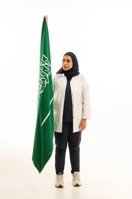 The concept of love for the homeland and belonging to it, Saudi Flag Day on March 11, National Day on September 23, a portrait of a Saudi Gulf Arab woman in a hijab wearing casual attire looking at the Kingdom's flag, participation in national holidays, full-body, white background.