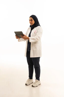 بورتريه من الجانب لامرأة عربية خليجية سعودية محجبة ترتدي الزى الكاجوال و شعار التوعيه بالكشف المبكر لسرطان الثدي تحمل التابلت بيدها، اليوم العالمي للتوعية بالامراض الخبيثة, الجسم بالطول الكامل, خلفية بيضاء