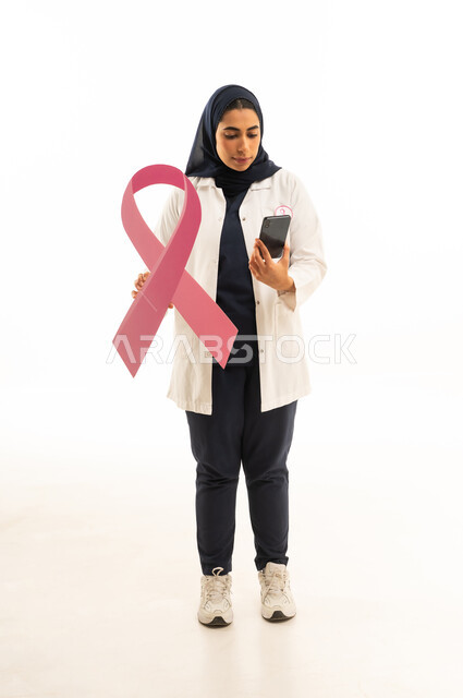 الحملة التوعويه بالامراض الخبيثه، شعار اليوم العالمي للتوعيه بالكشف المبكر لسرطان الثدي،   بوتريه لامرأة عربية خليجية سعودية محجبة ترتدي الزى الكاجوال تمسك بيديها شعار الحملة العالمية و الهاتف المحمول، خلفية بيضاء