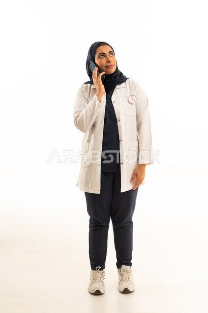 The slogan for the World Awareness Day for Early Detection of Breast Cancer, the awareness campaign for malignant diseases, looking towards the distant horizon with future perspectives, a portrait of a Saudi Gulf Arab woman in a hijab wearing casual attire talking on a mobile phone, white background.