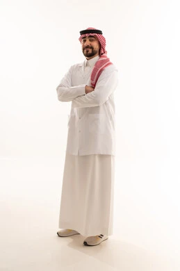 طبيب عربي خليجي سعودي يرتدي المعطف الابيض الطبي على الزي التقليدي للمملكة يقف شامخاً عاقداً ذراعيه , خلفية بيضاء , الجسم بالطول الكامل
