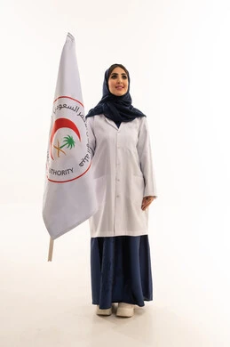 طبيبة عربية خليجية سعودية محجبة ترتدي عباءة زرقاء و المعطف الطبي الابيض ترفع علم هيئة الهلال الاحمر السعودي بسعادة بالغة , خلفية بيضاء , الجسم بالطول الكامل , النظر للاعلى