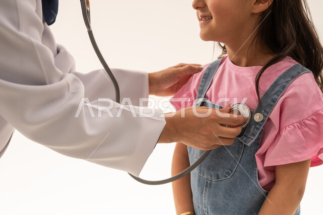 بورتريه مقرب لطبيبة القلب العربية السعودية الخليجية تقوم بعملها باتقان , طفلة عربية خليجية سعودية ترتدي الزي الكاجوال تقف بابتسامة لطيفة امام الطبيبة لاستكمال الفحص الدوري , خلفية بيضاء