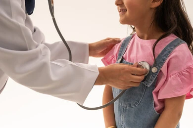 بورتريه مقرب لطبيبة القلب العربية السعودية الخليجية تقوم بعملها باتقان , طفلة عربية خليجية سعودية ترتدي الزي الكاجوال تقف بابتسامة لطيفة امام الطبيبة لاستكمال الفحص الدوري , خلفية بيضاء