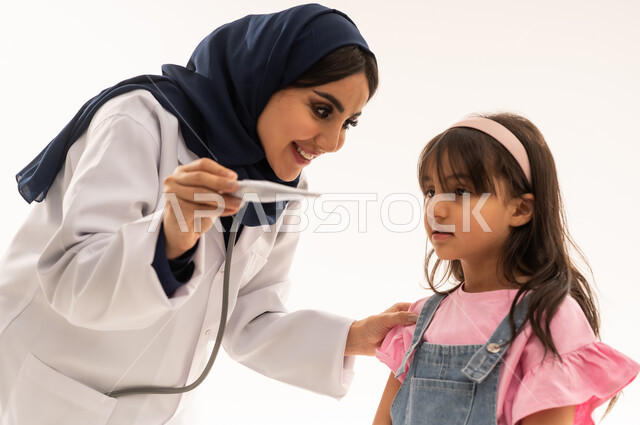 ايماءات السعادة بعد الاطمئنان على درجة حرارة الفتاة الصغيرة , طبيبة عربية سعودية خليجية ترتدي المعطف الطبي الابيض تعرض للطفلة الصغيرة الاخبار السعيدة , طفلة عربية خليجية سعودية ترتدي الزي الكاجوال تشاهد درجة الحرارة الطبيعية للجسد , بورتريه مقرب , خلفية بيضاء