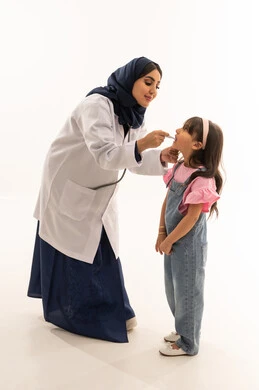 طبيبة عربية خليجية سعودية محجبة ترتدي عباءة زرقاء و معطف طبي ابيض تنحني امام الفتاة الصغيرة لمتابعة حالتها الصحية , طفلة عربية خليجية سعودية ترتدي الزي الكاجوال تقف امام الطبيبة اثناء قياس درجة الحرارة ’ بورتريه خلفية بيضاء , الجسم بالطول الكامل