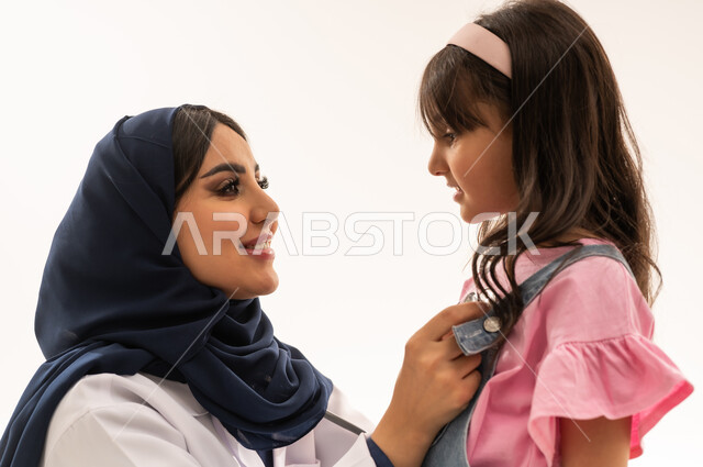 علاقات ثقة متبادلة ومحبة بين الاطباء و المرضى , طبيبة عربية خليجية سعودية ترتدي المعطف الطبي الابيض تستمع بانصات الى دقات قلب الفتاة الصغيرة , طفلة عربية خليجية سعودية ترتدي الزي الكاجوال تتابع حالة قلبها , بورتريه مقرب , خلفية بيضاء