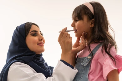 متابعة  درجة حرارة الجسد الطبيعية من الضروريات الاساسية خلال فحص الاطفال , طبيبة عربية خليجية سعودية ترتدي المعطف الابيض الطبي تحمل مقياس درجة الحرارة ,طفلة عربية خليجية سعودية ترتدي الزي الكاجوال تقف امام الطبيبة في ثبات , بورتريه مقرب , خلفية بيضاء