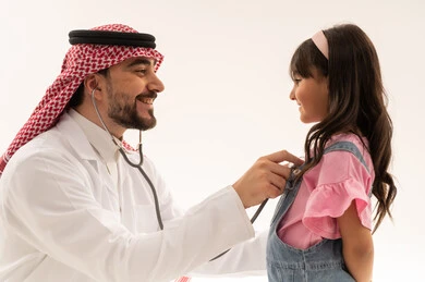 Performing regular check-ups happily, an Arab Gulf Saudi doctor wearing a white medical coat listens attentively to the heartbeat of a young girl, an Arab Gulf Saudi child dressed in casual attire checking on her heart health, close-up portrait, white background.