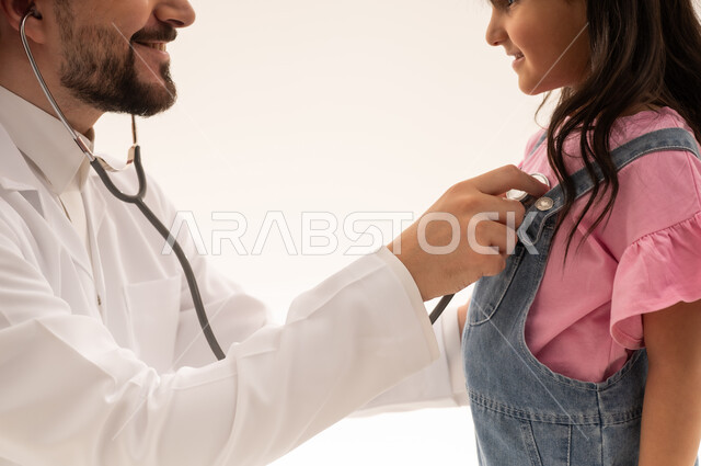 جميع التخصصات متوفرة في هيئة الهلال الاحمر السعودي بكفاءة عالية , طبيب عربي سعودي خليجي يرتدي المعطف الابيض الطبي يستمع الى ضربات قلب الفتاة الصغيرة , طفلة عربية خليجية سعودية ترتدي الزي الكاجوال تقف امام الطبيب الكفء لمتابعة حالة القلب , ايماءات السعادة , بورتره مقرب , خلفية بيضاء