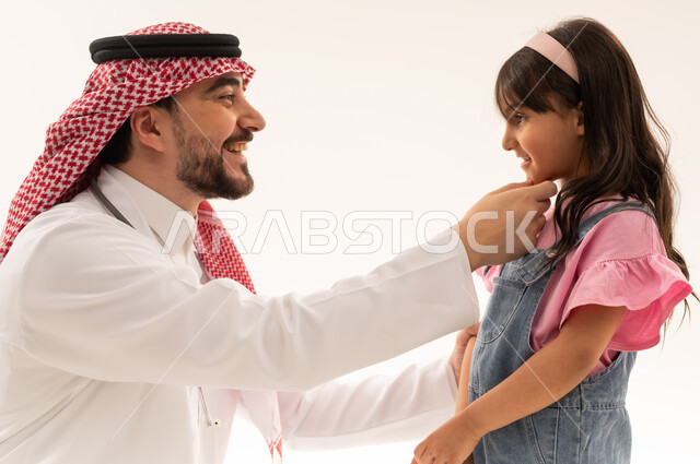 بورتريه مقرب ملئ بالبهجة و السعادة بين الطبيب و الفتاة الصغيرة , طبيب عربي خليجي سعودي يرتدي المعطف الطبي الابيض يمازح الطفلة , طفلة عربية خليجية سعودية ترتدي الزي الكاجوال تبتسم للطبيب بعد انتهاء الفحص و الاطمئنان على الصحة العامة , خلفية بيضاء