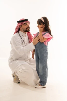 طفلة عربية خليجية سعودية ترتدي الزي الكاجوال تشير الى الاذن ليتم فحصها , طبيب عربي خليجي سعودي يرتدي معطف ابيض طبي يستمع بانصات الى شكوى الفتاة الصغيرة , بورتريه خلفية بيضاء , الجسم بالطول الكامل