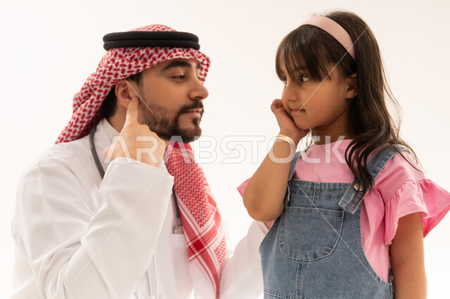 الفحص المبكر على حاسة السمع و قياس قوة السمع خدمة متوفرة في هيئة الهلال الاحمر السعودي , طبيب عربي سعودي خليجي يرتدي المعطف الطبي الابيض يجلس بجانب الفتاة لفحص الاذن , طفلة عربية خليجية سعودية ترتدي الزي الكاجوال تشير الى اذنها , بورتريه مقرب , خلفية بيضاء
