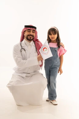 ايماءات السعادة و البهجة واضحة على الطبيب و الفتاة الصغيرة , طبيب عربي خليجي سعودي يرتدي معطف طبي ابيض يجلس القرفصاء بجانب الطفلة الصغيرة , طفلة عربية خليجية سعودية ترتدي الزي الكاجوال ترفع راية الهلال الاحمر السعودي بفخر و عزة , بورتريه خلفية بيضاء , الجسم بالطول الكامل