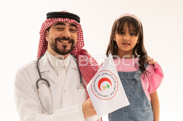 طبيب عربي سعودي خليجي يرتدي الزي التقليدي في المملكة يحمل راية هيئة الهلال الاحمر السعودي البيضاء , طفلة عربية خليجية سعودية ترتدي الزي الكاجوال تقف بسعادة بجانب الطبيب الكفء , بورتريه مقرب , خلفية بيضاء