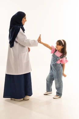A good relationship between doctors and patients, a Saudi Arabian Gulf Arab female doctor in a hijab wearing a white medical coat shakes hands with a little girl cheerfully, an Arab Gulf Saudi girl in casual attire playfully interacts with the doctor with kindness and happiness, portrait with a white background, full body.