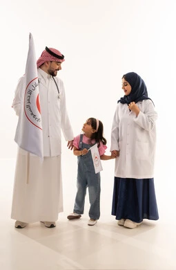 The relationships of love and mutual affection between the members of the Saudi Red Crescent Authority and the patients, a Gulf Arab Saudi girl standing between the Saudi doctor and doctor, looking at him with pride and confidence, an Arab Gulf Saudi doctor wearing the traditional dress in the Kingdom and raising the Saudi Red Crescent flag, an Arab Saudi female doctor in a hijab wearing a white medical coat looking at the little girl with gestures of love and happiness, portrait with a white ba