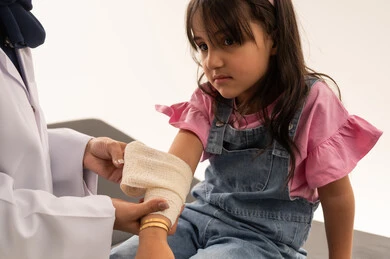 طفلة عربية خليجية سعودية تشعر بالحزن اثناء تلقي العلاج , طبيبة عربية خليجية سعودية تقوم بوضع ضمادة لثبيت العظام على ذراع الفتاة الصغيرة , بورتريه مقرب , خلفية بيضاء