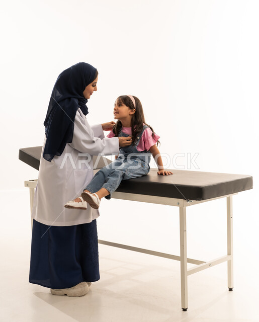 اختيار الكفاءات المدربة بعناية في هيئة الهلال الاحمر السعودي , طفلة عربية خليجة سعودية ترتدي الزي الكاجوال تجلس على سرير كشف اسود , طبيبة عربية خليجية سعودية ترتدي معطف طبي ابيض تستمع بانصات لنبضات قلب الفتاة , بورتريه خلفية بيضاء , الجسم بالطول الكامل