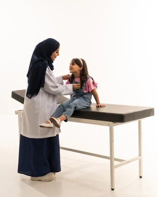 اختيار الكفاءات المدربة بعناية في هيئة الهلال الاحمر السعودي , طفلة عربية خليجة سعودية ترتدي الزي الكاجوال تجلس على سرير كشف اسود , طبيبة عربية خليجية سعودية ترتدي معطف طبي ابيض تستمع بانصات لنبضات قلب الفتاة , بورتريه خلفية بيضاء , الجسم بالطول الكامل