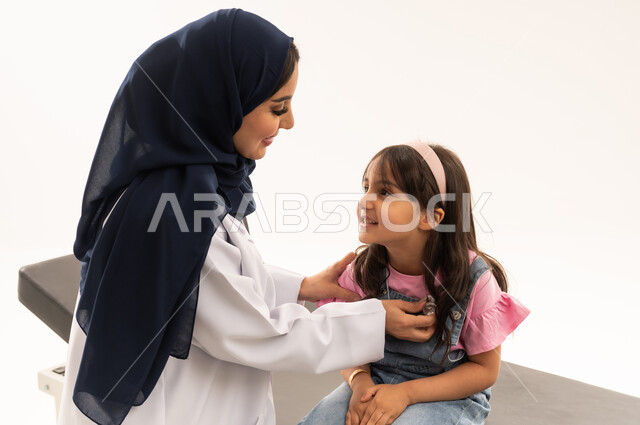 الفحوصات الدورية على القلب خدمات متاحة في هيئة الهلال الاحمر السعودي ,طبيبة عربية خليجية سعودية محجبة ترتدي المعطف الابيض الطبي تقوم بفحص صحة القلب , طفلة عربية خليجية سعودية ترتدي الزي الكاجوال تجلس بهدوء على سرير الكشف , بورتريه مقرب , خلفية بيضاء