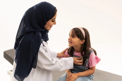 الفحوصات الدورية على القلب خدمات متاحة في هيئة الهلال الاحمر السعودي ,طبيبة عربية خليجية سعودية محجبة ترتدي المعطف الابيض الطبي تقوم بفحص صحة القلب , طفلة عربية خليجية سعودية ترتدي الزي الكاجوال تجلس بهدوء على سرير الكشف , بورتريه مقرب , خلفية بيضاء