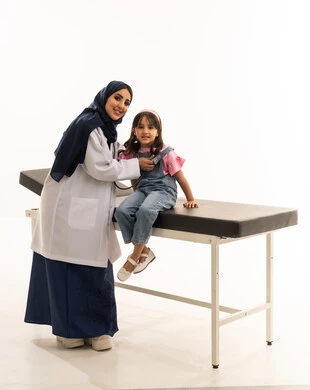 النظر للكاميرا مع ايماءات السعادة و الطمأنينة ,طبيبة عربية خليجية سعودية محجبة ترتدي المعطف الابيض الطبي تستمع بانصات الى نبضات قلب الفتاة الصغيرة , طفلة عربية خليجية سعودية ترتدي الزي الكاجوال تجلس على سرير الكشف اثناء الفحص الدوري للقلب , بورتريه خلفية بيضاء , الجسم بالطول الكامل