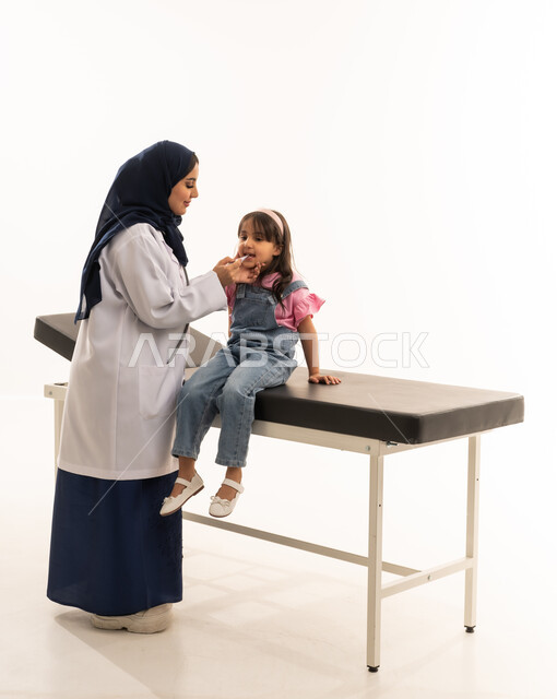 الفحص الطبي الشامل للاطفال الصغار , طفلة عربية خليجية سعودية ترتدي الزي الكاجوال تجلس على سرير الكشف في العيادة , طبيبة عربية خليجية سعودية محجبة ترتدي المعطف الطبي الابيض تقوم بقياس درجة حرارة الفتاة الصغيرة للتأكد من سلامتها , بورتريه خلفية بيضاء , الجسم بالطول الكامل