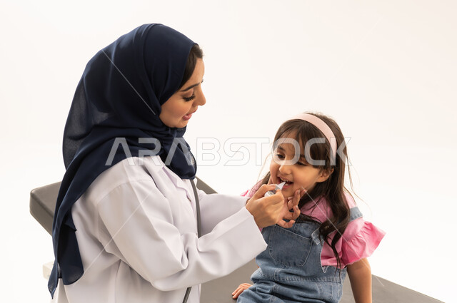 تطعيمات سنوية وشهرية ضرورية مجانية للاطفال الصغار في هيئة الهلال الاحمر السعودي , طفلة عربية خليجية سعودية ترتدي الزي الكاجوال تجلس على سرير الكشف تتلقى الجرعة المناسبة من التطعيم  , طبيبة عربية خليجية سعودية محجبة ترتدي المعطف الطبي الابيض تتابع حالة الفتاة الصغيرة قبل اعطاء التطعيم المناسب , بورتريه مقرب , خلفية بيضاء