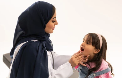 العناية بالاسنان منذ الصغر والحفاظ عليها من التسوس , طفلة عربية خليجية سعودية ترتدي الزي الكاجوال تجلس على سرير الكشف في عيادة فحص الاسنان , طبيبة عربية خليجية سعودية محجبة ترتدي المعطف الطبي الابيض تقوم بالكشف عن امراض اللثة و الفم ,بورتريه مقرب , خلفية بيضاء